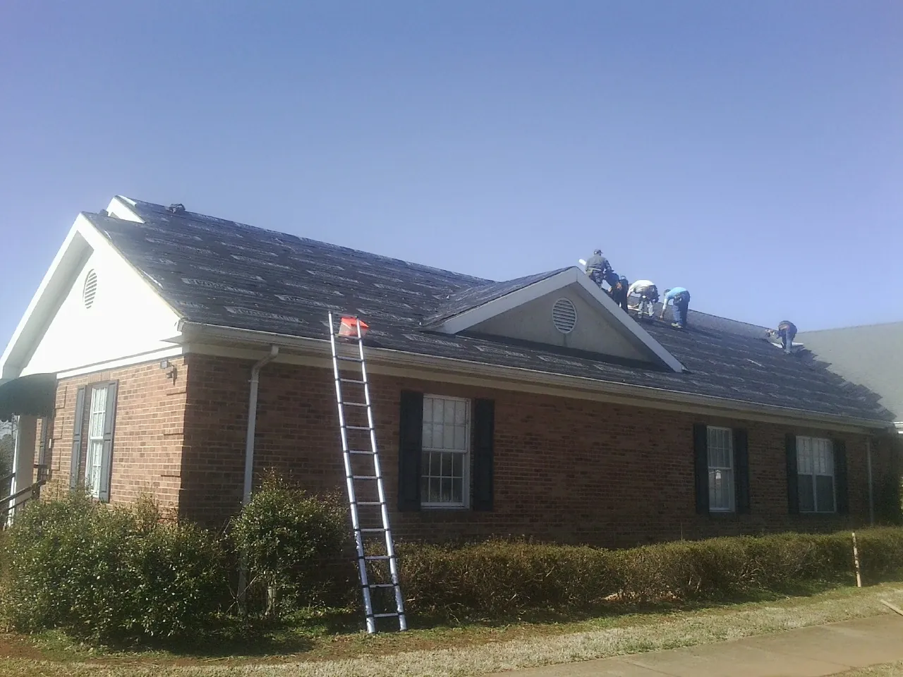 Crew tearing shingles off a brick ranch roof with a ladder set — Emergency Roof Repair work by our crew in Othello