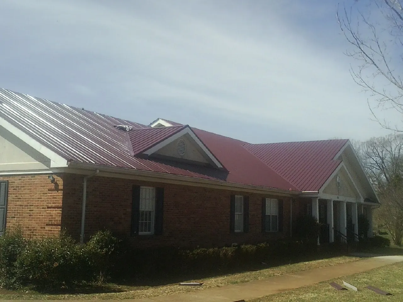 Red metal roof with gabled entries on a long brick building, from a Hail Damage Roof Repair job in Othello