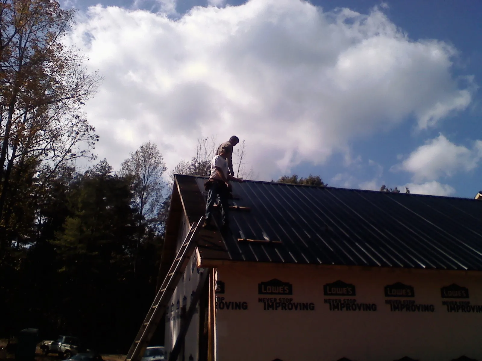 Roofer fastening dark metal panels high against a cloudy sky, from a Roof Inspection job in Othello